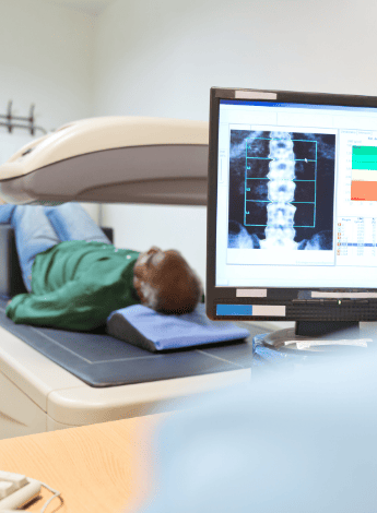 The image is looking over someone's shoulder to see a computer screen. The screen is showing the spin of a patient who is lying on an X-ray platform. 